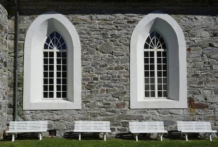 Quelle: Martin Bergmann Zwei Kirchenfenster von außen mit vier Bänken davor