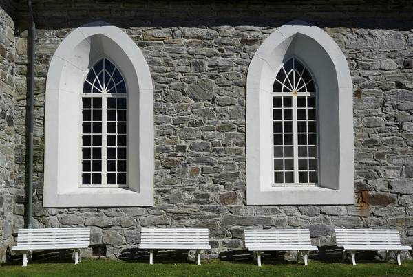 Zwei Kirchenfenster von außen mit vier Bänken davor
