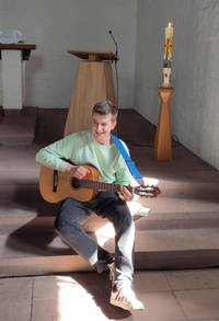 Ein junger Mann sitzt  in der Kirche vor dem Altarraum und spielt Gitarre.